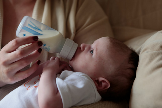 Newborn drinking expressed breast milk from a bottle while being held by a parent